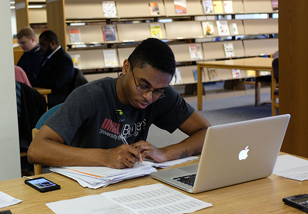 Student in the library in front of notes and a laptop