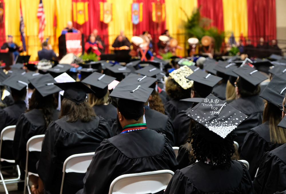A crowd of students in full regalia listening to a graduation commencement address