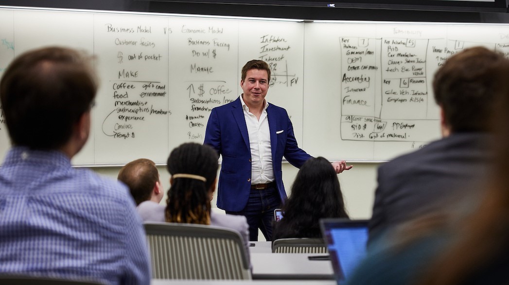 A professor standing in front of a whiteboard gives an accounting lecture to a classroom of students
