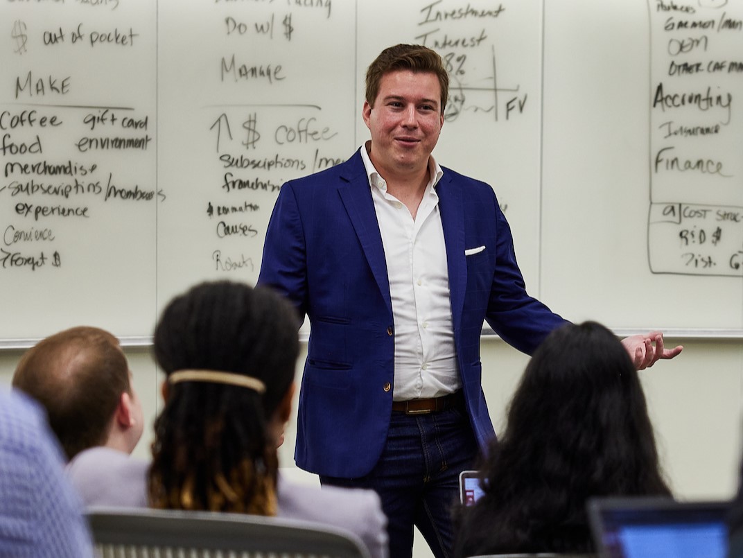 A professor standing in front of a whiteboard gives an accounting lecture to a classroom of students