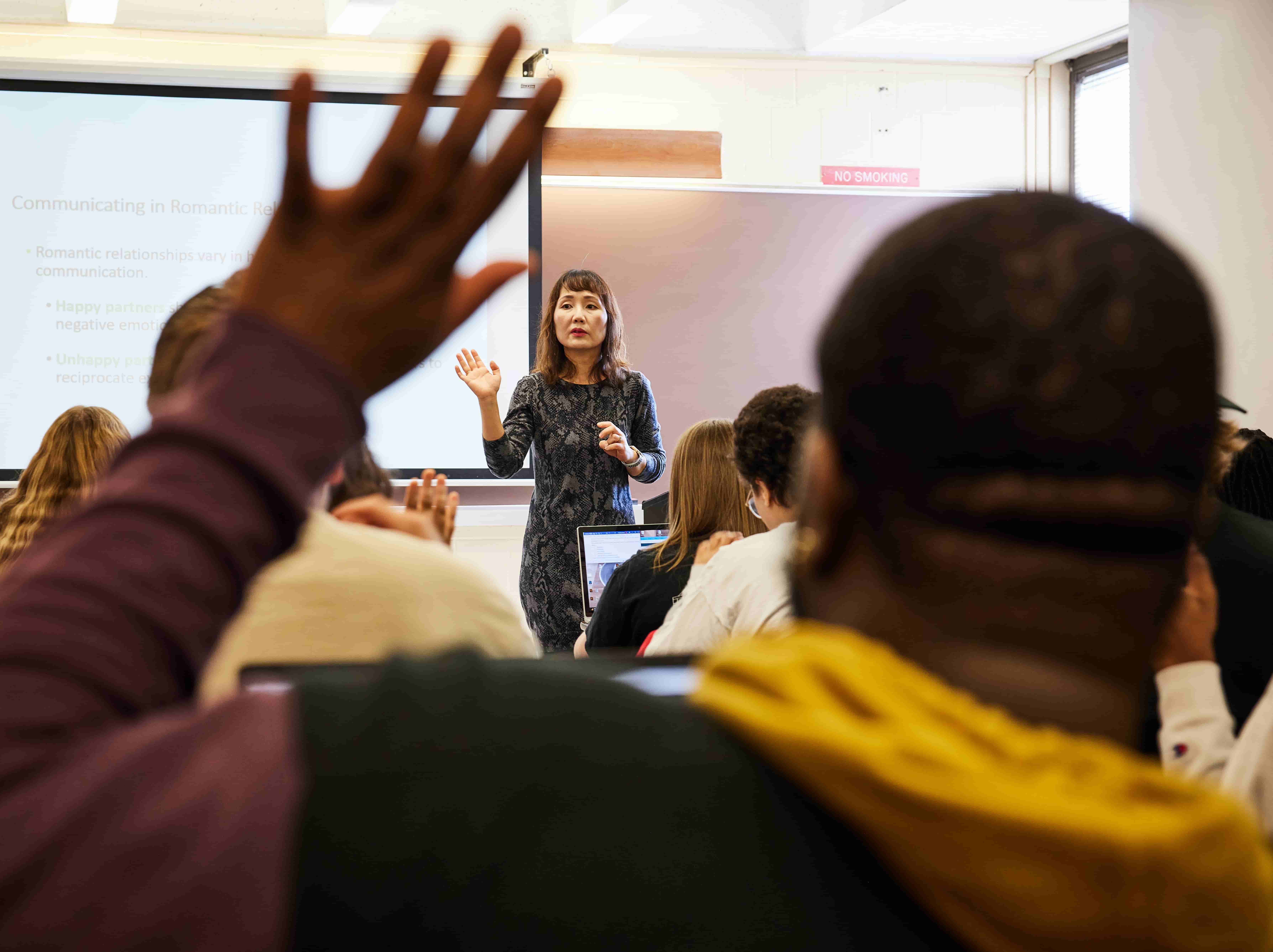 A student in class raises their hand in front of the professor
