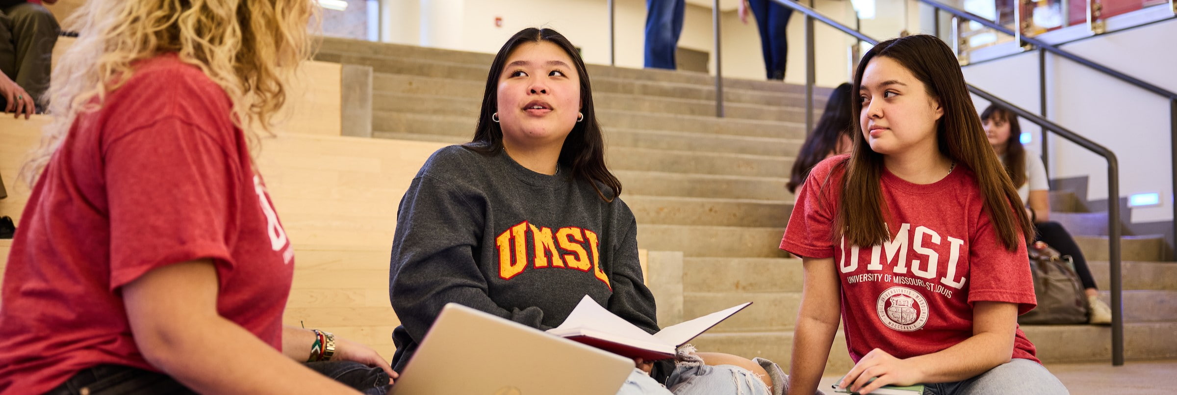 Three students converse while sitting on the steps of a lobby