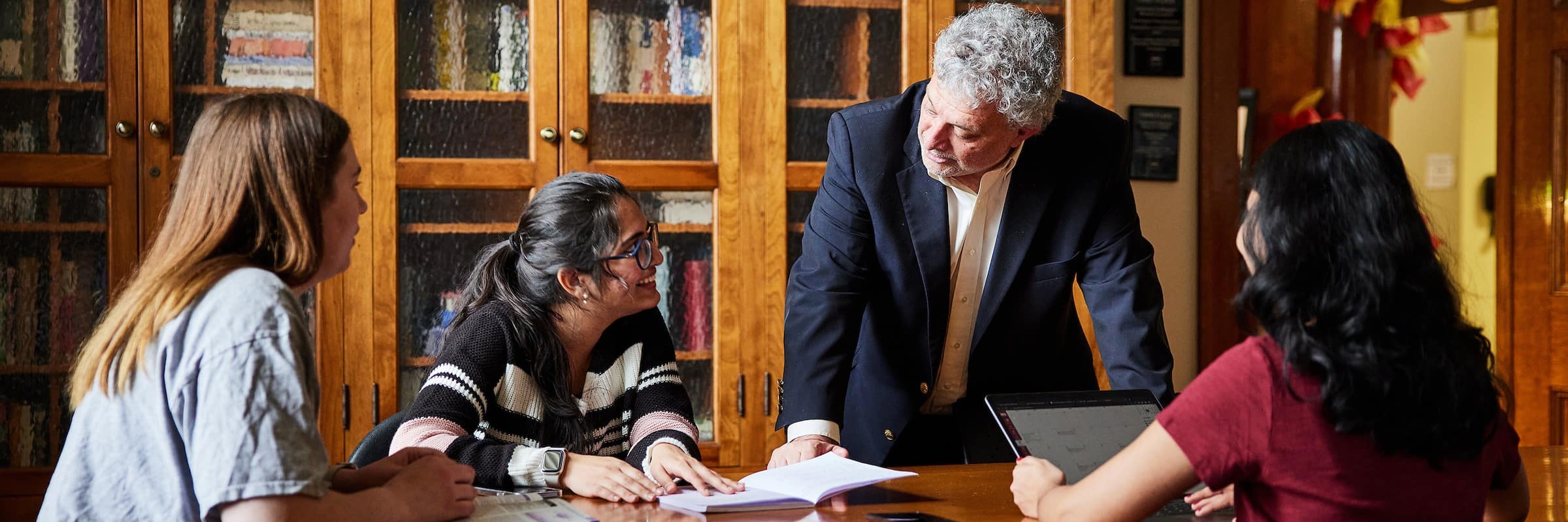 A professor leans over a table to answer questions from a group of students