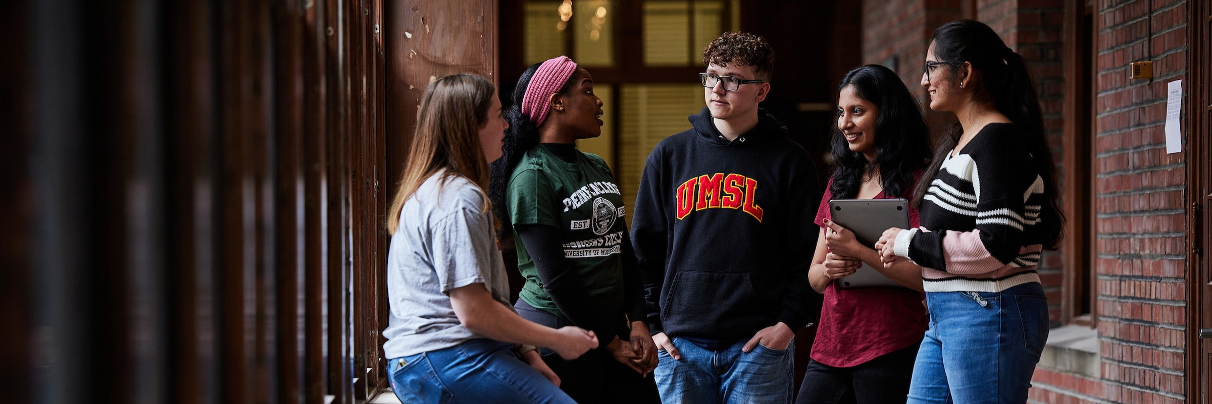 Five students converse in the hall of an academic building