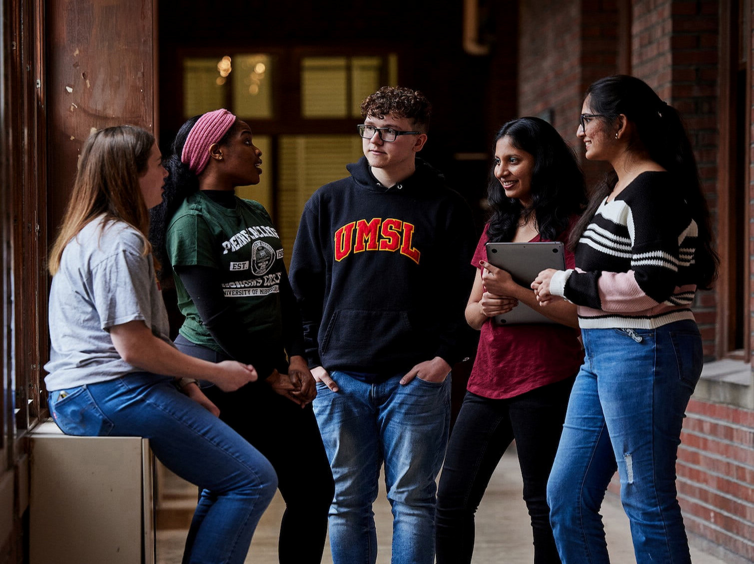 Five students converse in the hall of an academic building