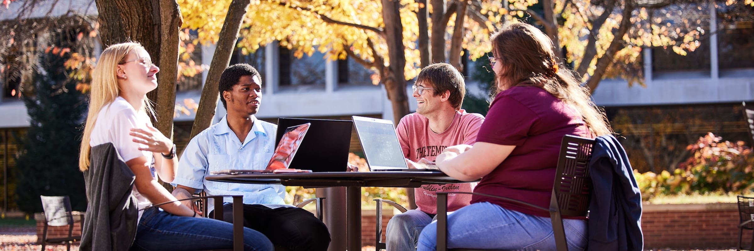 Four students converse at a roundtable outside