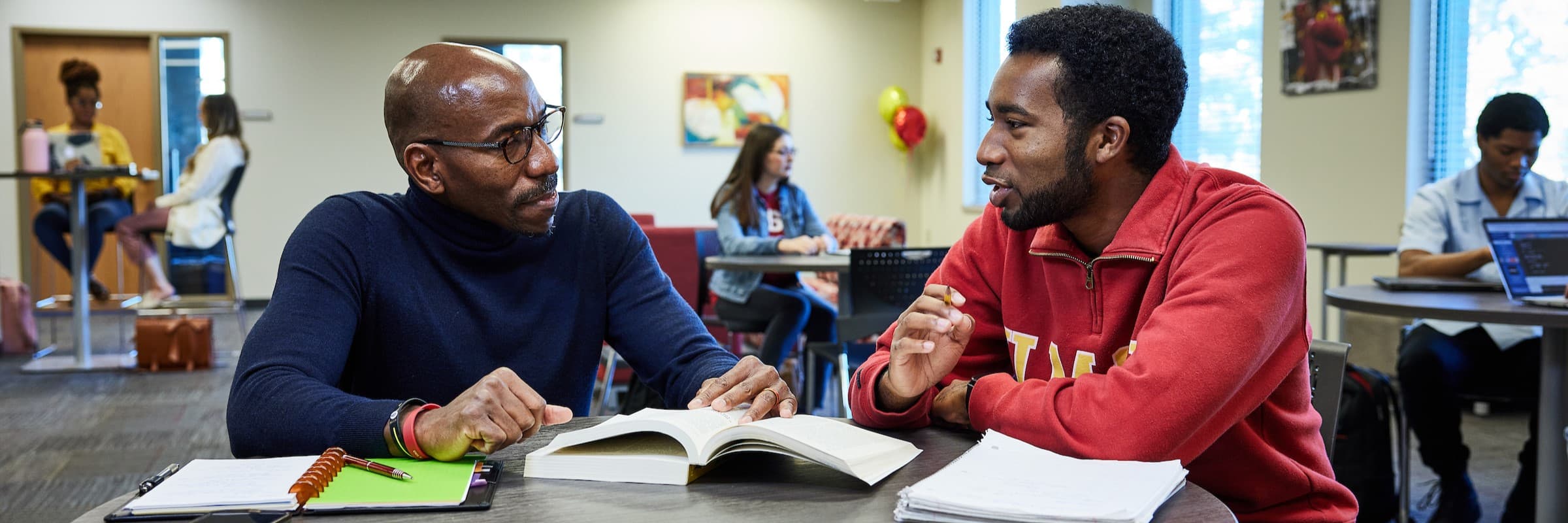 In a study room, two students discuss notes from a class