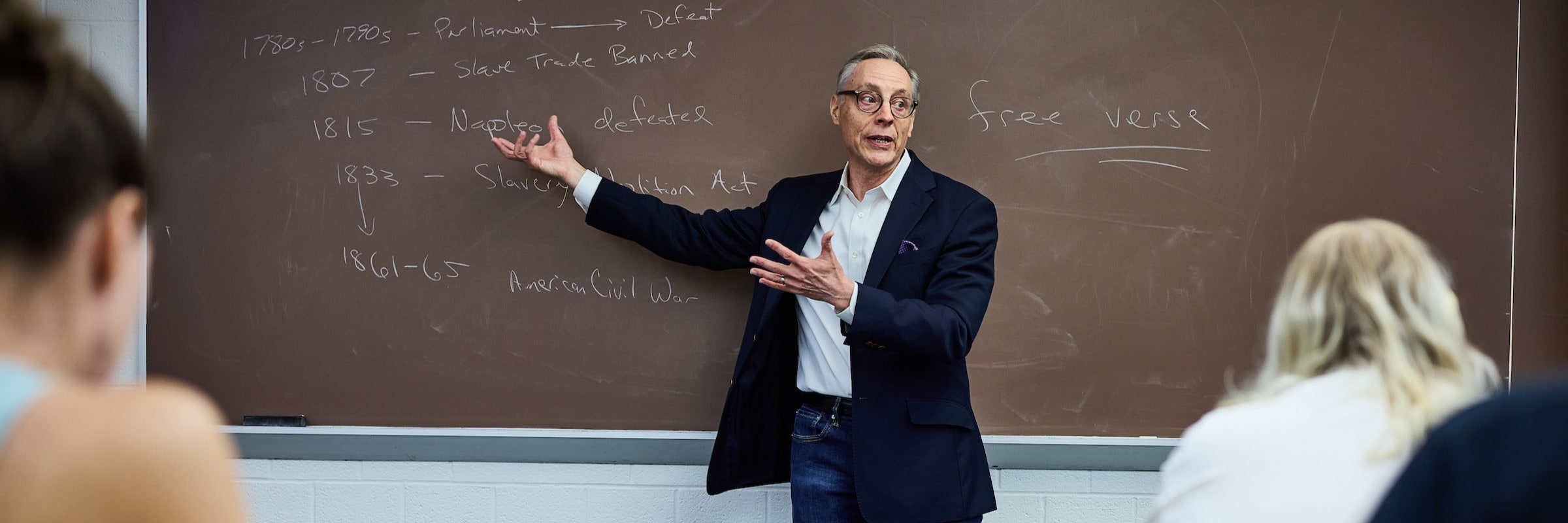 A professor gives a lecture in front of a chalkboard