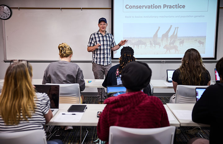 in a classroom, professor by slides at the front of the room
