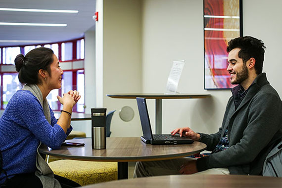 two students, one with laptop, sitting at a table