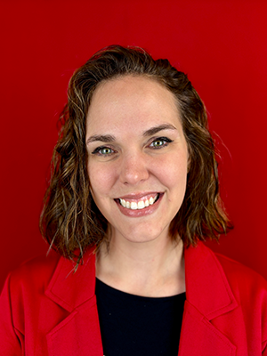 Close-up photo of Kat Riddler wearing a red blazer in front of a red background.