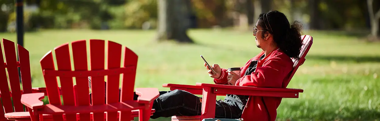 student with a phone sitting outside on campus in a red chair