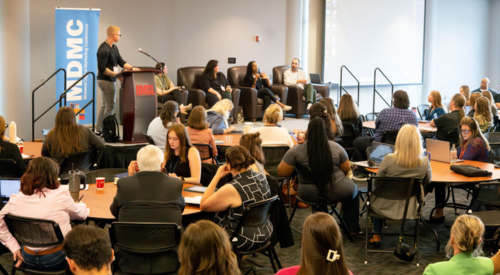 a group of people sitting down at a conference with five people on stage 