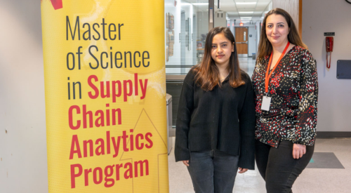 two women standing next to a yellow banner