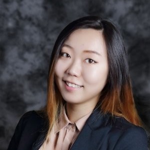 Professional headshot of a smiling woman in a dark blazer against a gray studio background.