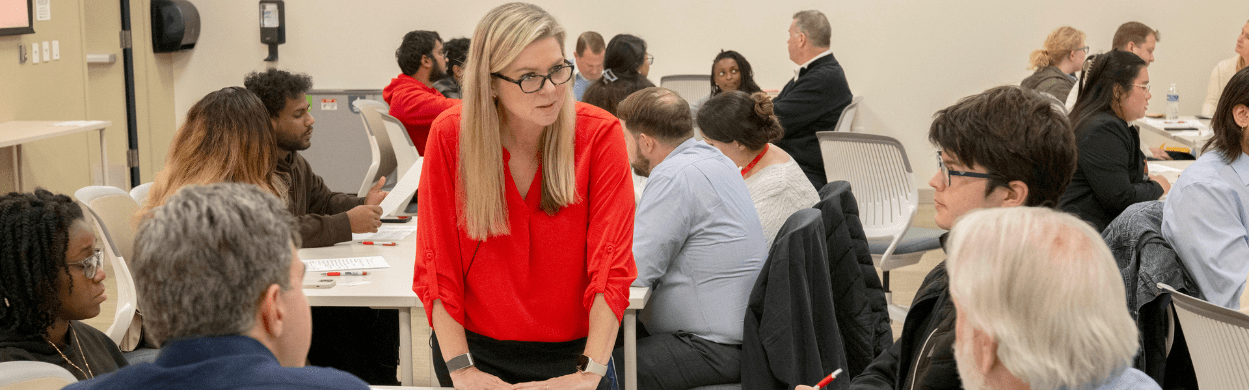 a woman talking to a group of people sitting at a table
