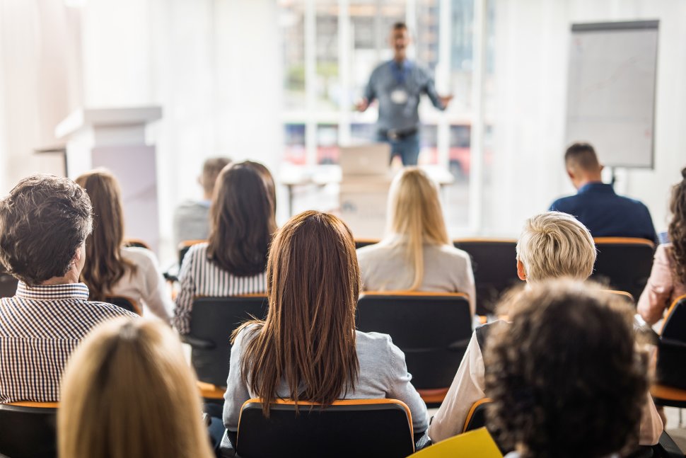 Man at the front of a classroom gives a lecture to people sitting in front of him