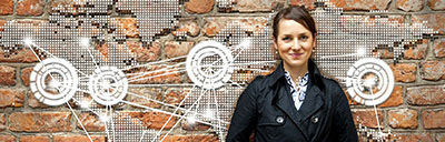 female student standing in front of brick wall with a world map