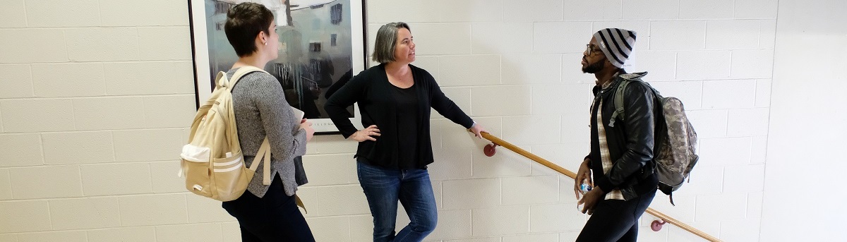 two students talking with a professor in a hallway