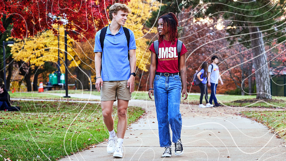 Two UMSL students walking along a pathway engaged in conversation