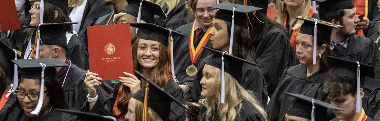 Graduate holding up their degree folder in a sea of other graduates