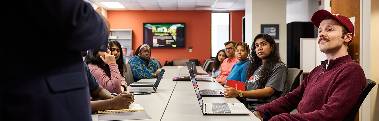 UMSL students around a table listening to a professor