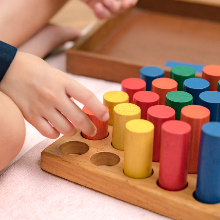 A child’s hand selecting a colorful wooden block from a sorting toy.