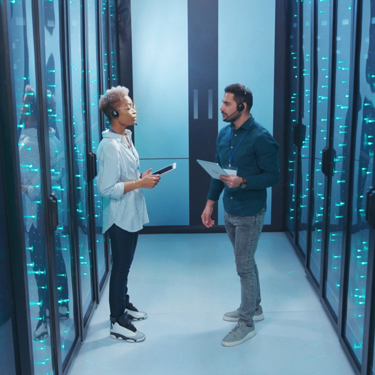 A modern data center scene featuring two professionals discussing while surrounded by server racks illuminated with blue lights.