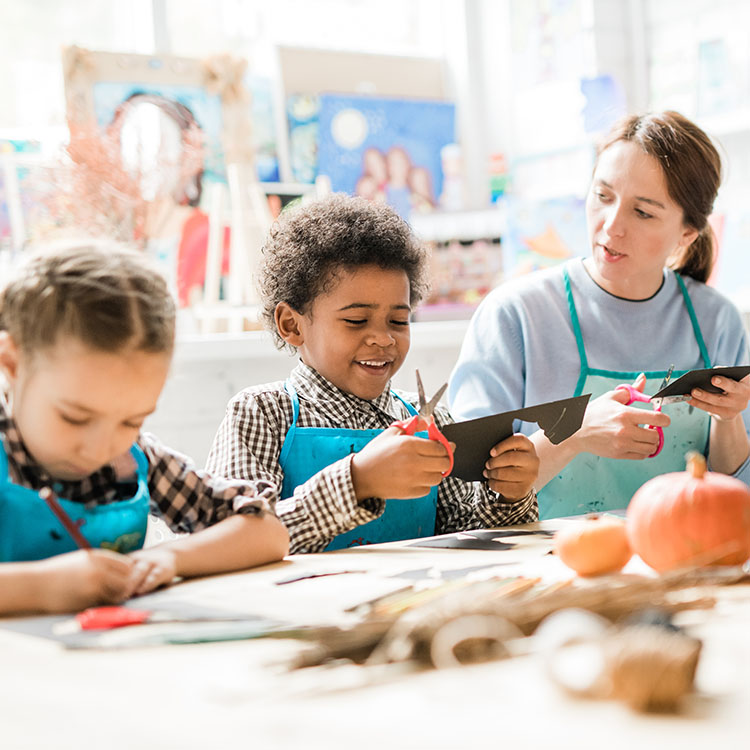 two young students and a teacher cutting paper