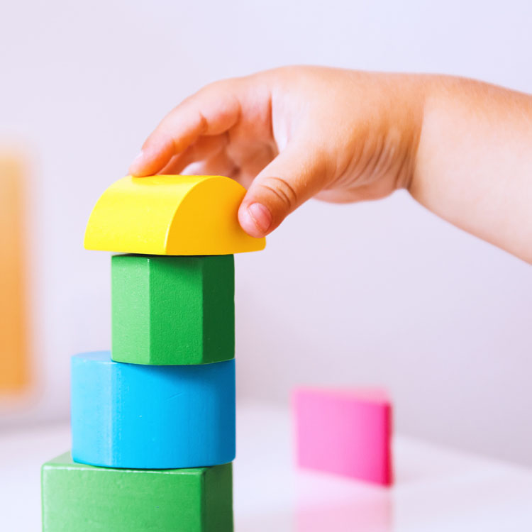 A child's hand stacking colorful building blocks in a playful arrangement.