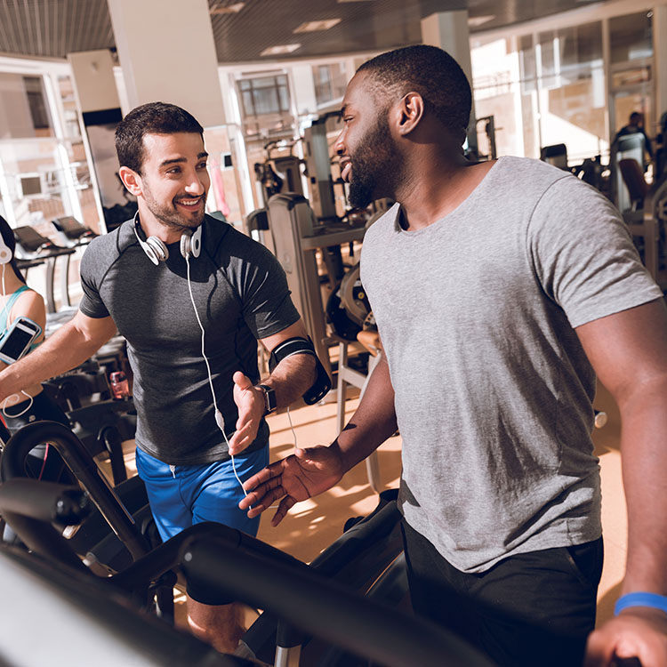 Two men engaged in a friendly conversation while working out in a gym. They appear to be enjoying their exercise routine together.