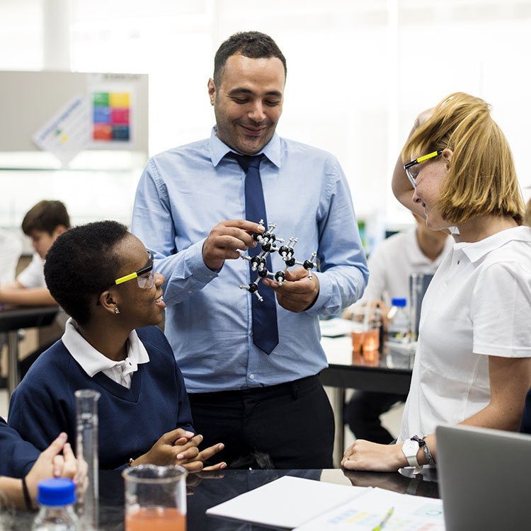 A teacher demonstrates a molecular model to engaged students in a science lab setting.