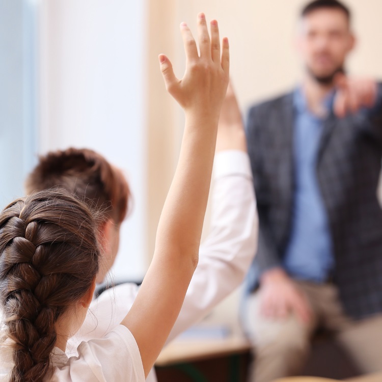 A classroom scene with a student raising their hand to ask a question while a teacher gestures towards them.