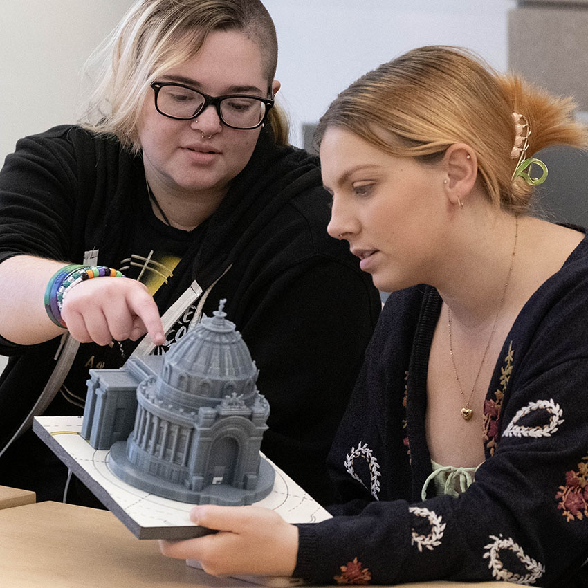 Two students examining a detailed architectural model of a dome structure during a hands-on learning session.