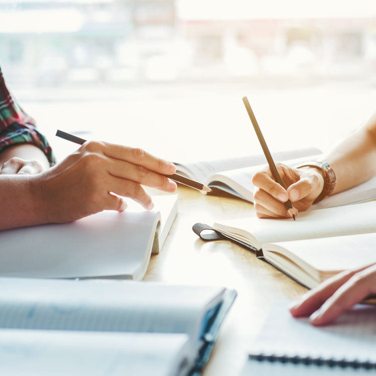 Two hands hold pens over notebooks, suggesting collaboration and brainstorming in a study or planning session.