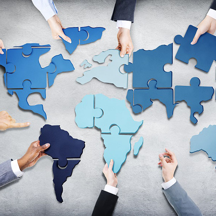Diverse hands connecting blue puzzle pieces shaped like continents, symbolizing collaboration and global unity.
