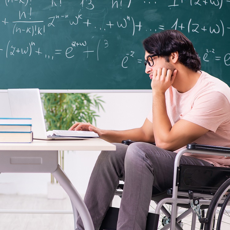 A student in a wheelchair engaged in online learning, sitting at a desk with a laptop and books, in front of a chalkboard filled with mathematical equations.