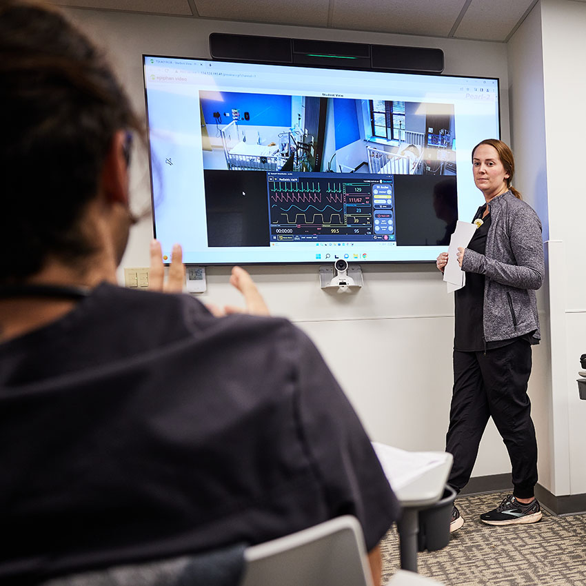 UMSL Instructor explaining medical data on a large screen to students in a classroom setting.