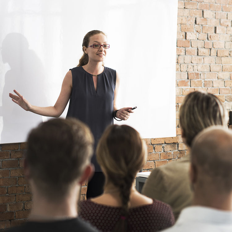 A woman giving a presentation to an audience in a brick-walled room.