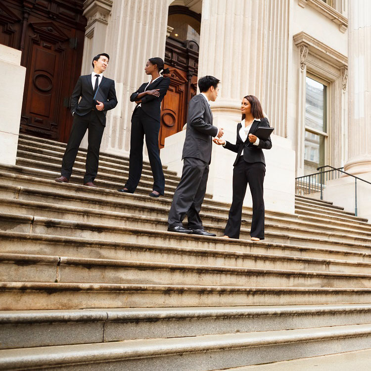 A group of four professionals in business attire conversing on the steps of a grand building.