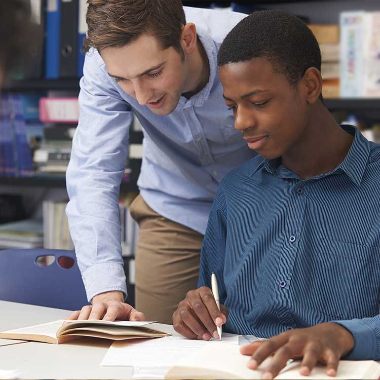 A teacher assisting a student with their studies at a desk, highlighting a supportive learning environment.