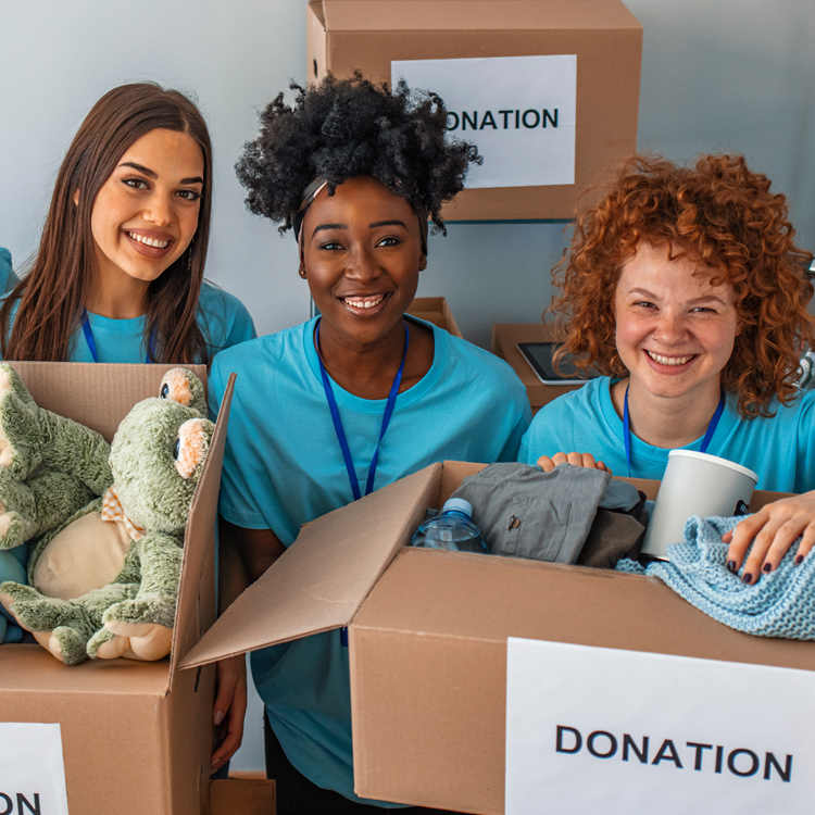 Three smiling volunteers holding donation boxes filled with clothes and toys.