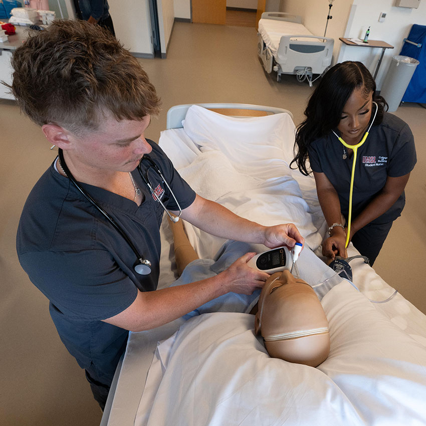 Two nursing students practice patient assessment on a training mannequin in the Sim lab.