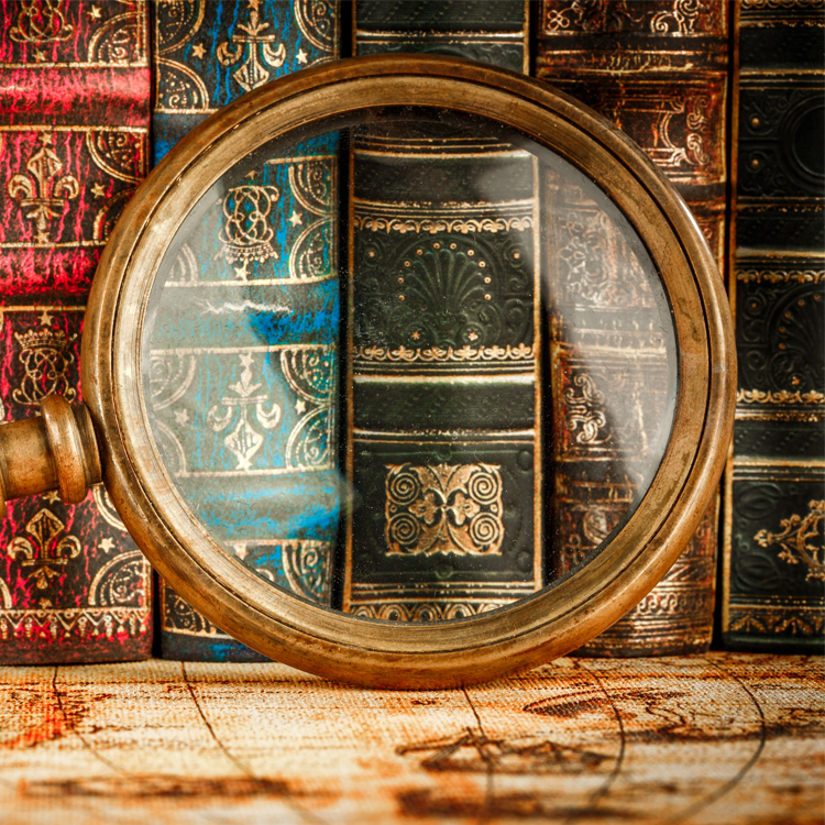 A vintage magnifying glass positioned over colorful, ornate book spines.