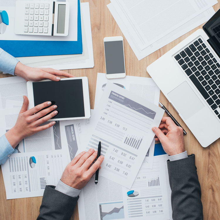 Aerial view of professionals collaborating with financial documents, a laptop, and mobile devices on a wooden desk.