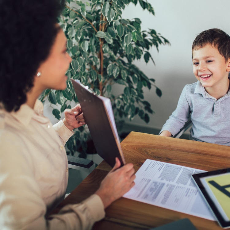 A woman engaging in a friendly conversation with a young boy during a meeting, with documents and a clipboard on the table.