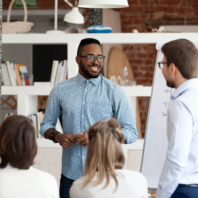 A smiling presenter engages an audience during a workshop, highlighting teamwork and collaboration in a modern office setting.