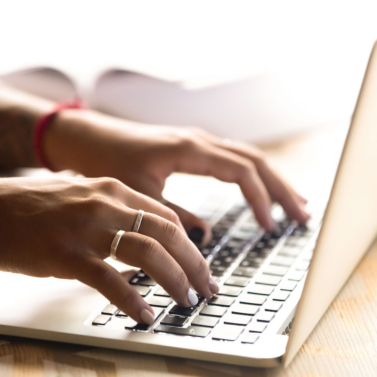 A close-up of hands typing on a laptop keyboard, showcasing a modern workspace environment.
