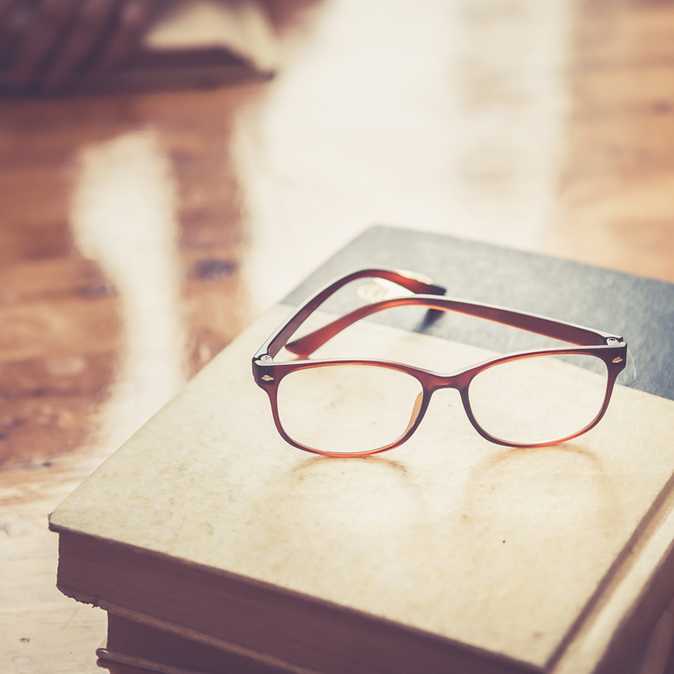 A pair of stylish brown and orange reading glasses resting on top of a stack of books.