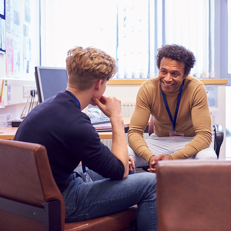 A counselor engages in a conversation with a young man in an office setting, emphasizing support and connection.